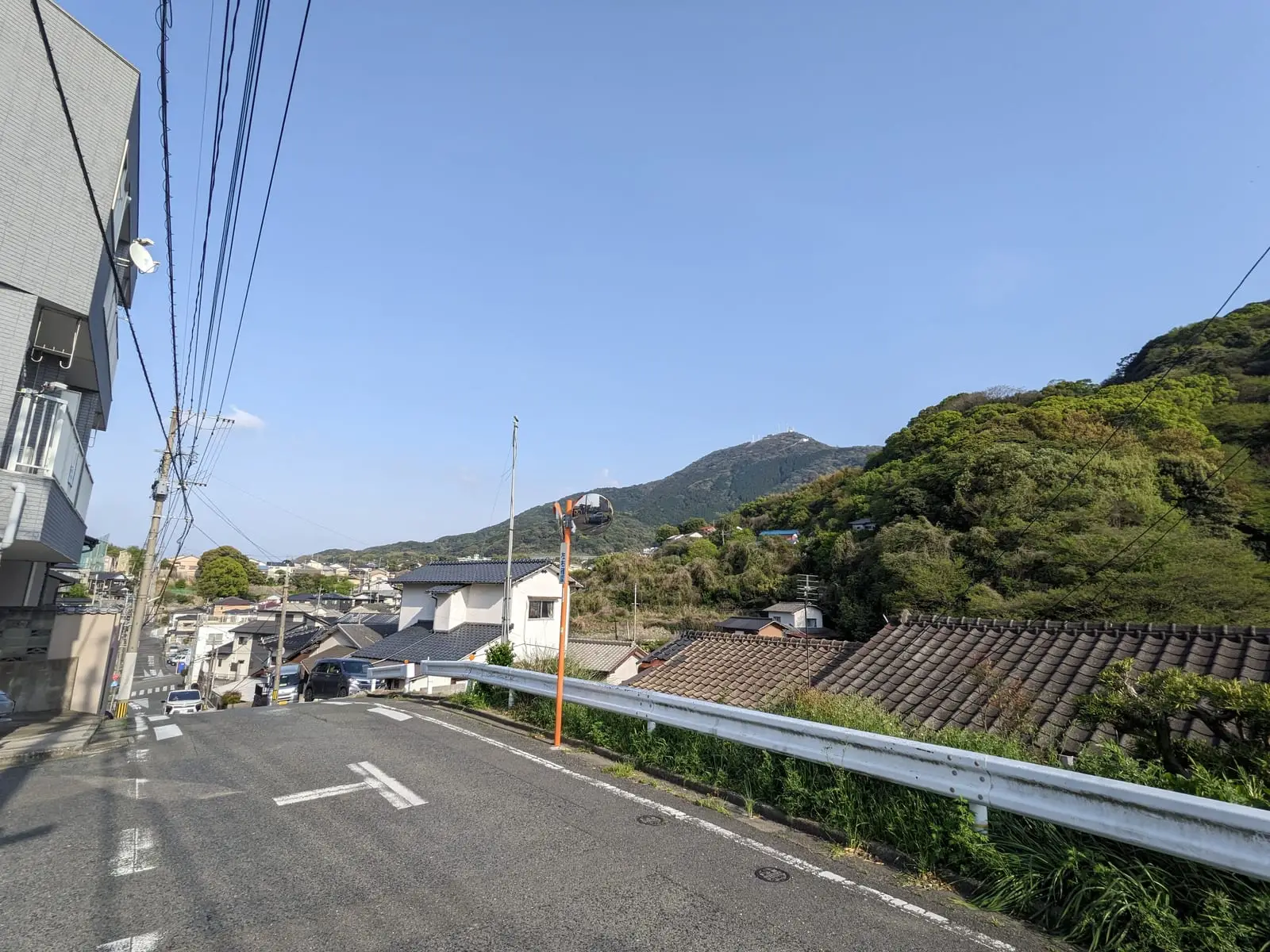 A quiet paved village road curving between houses with mountains and utility poles behind