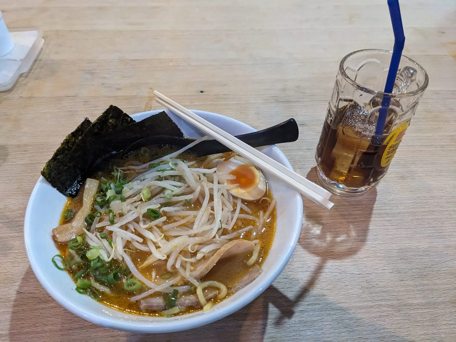 A bowl of ramen topped with nori and a boiled egg, beside an iced drink with a straw