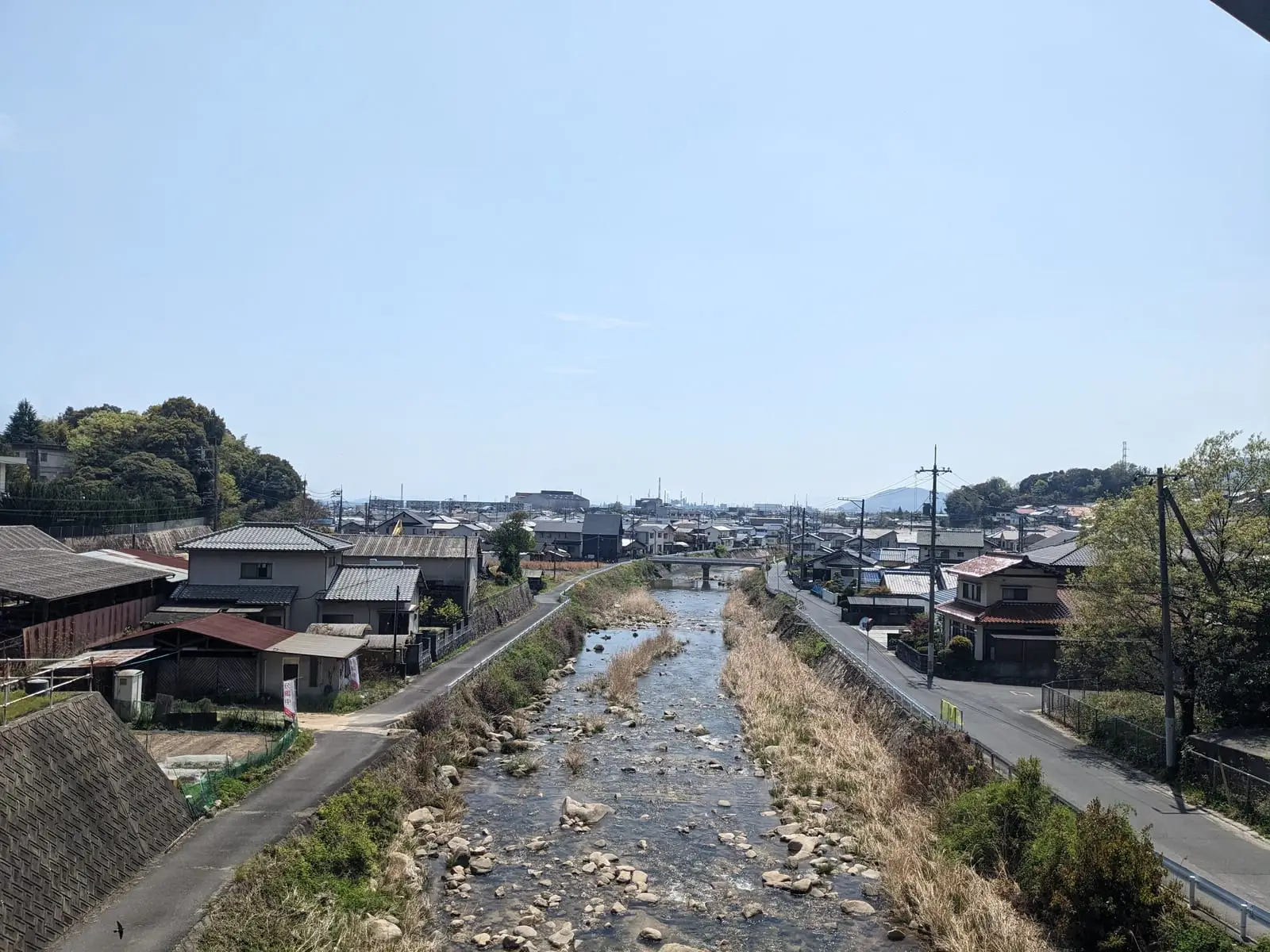 A view along a river through a small town, with houses on the bank and a road bridge crossing