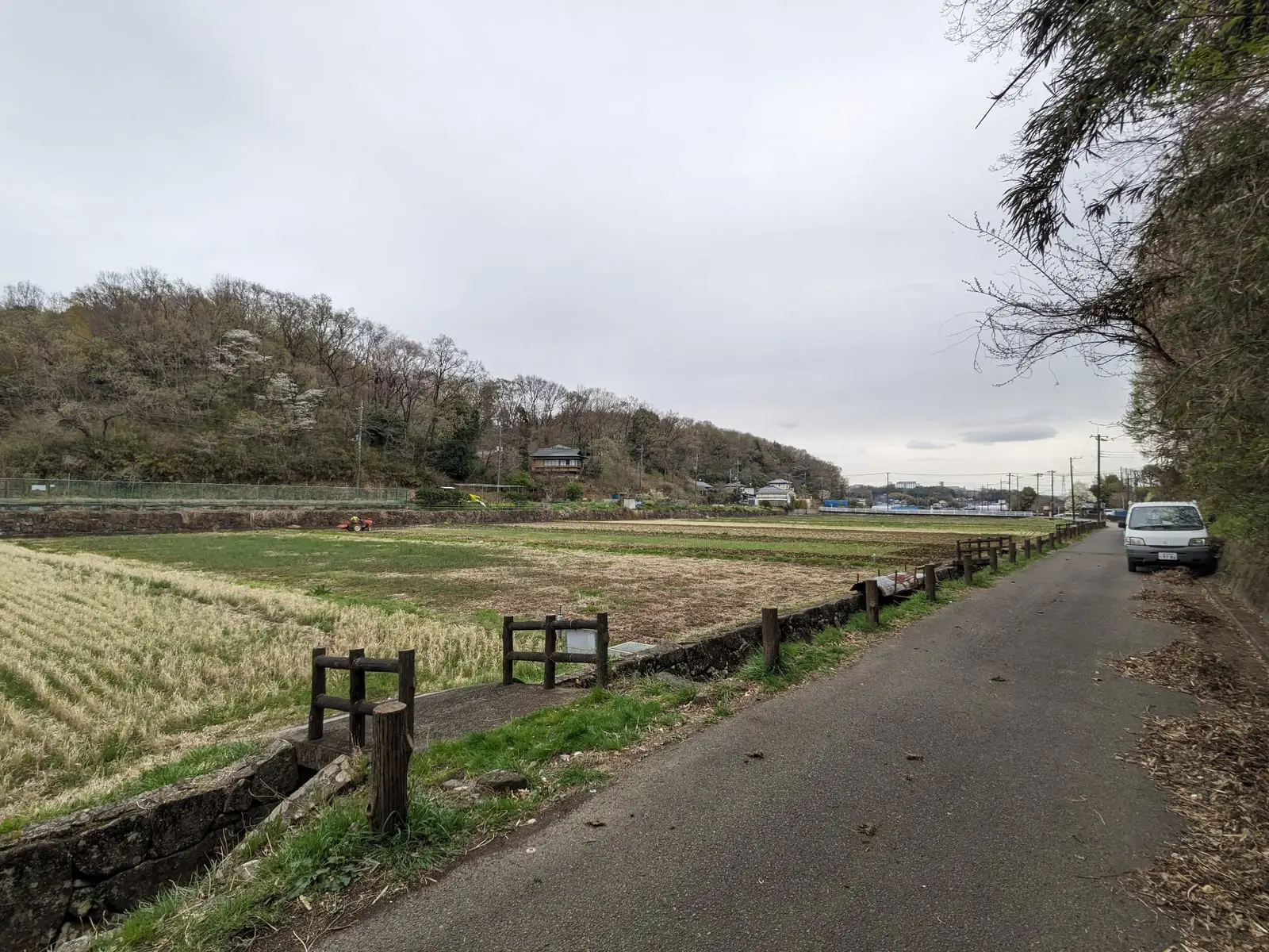 A quiet rural road running beside an open field, with a car parked in the distance