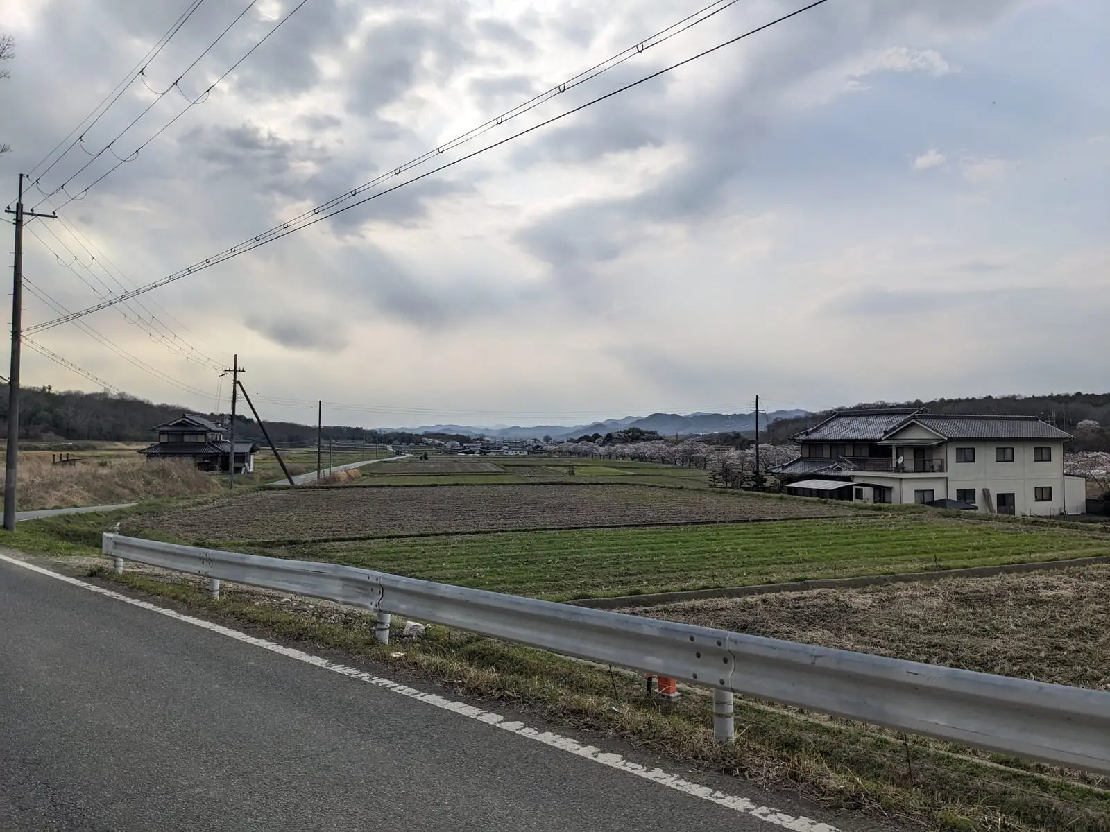 A rural road running between village houses, with hills visible under a grey sky