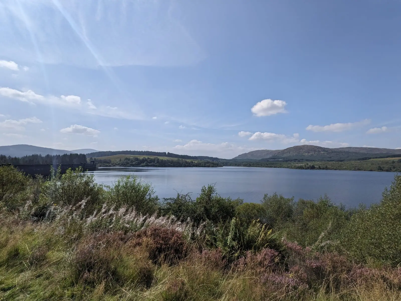 A loch surrounded by low Scottish hills beneath a blue sky
