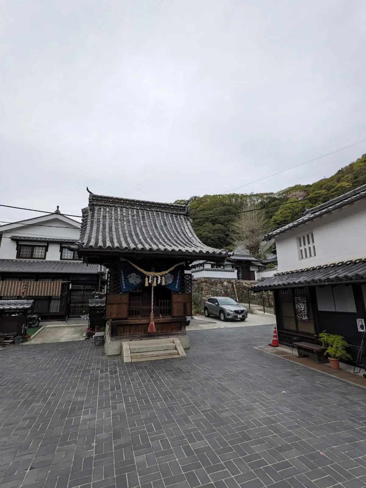 A wooden shrine gate and small shrine building beside a parked car in a residential street