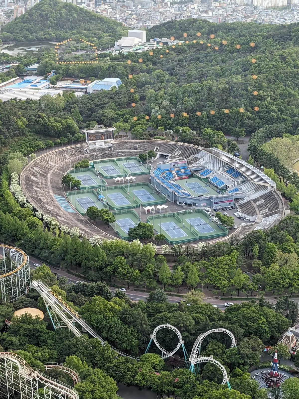 An aerial view of a stadium complex with several tennis courts, including one enclosed in its own miniature stadium
