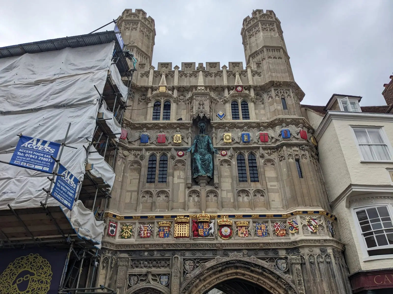 A green statue above a heraldic stone gateway in Canterbury, beside scaffolding