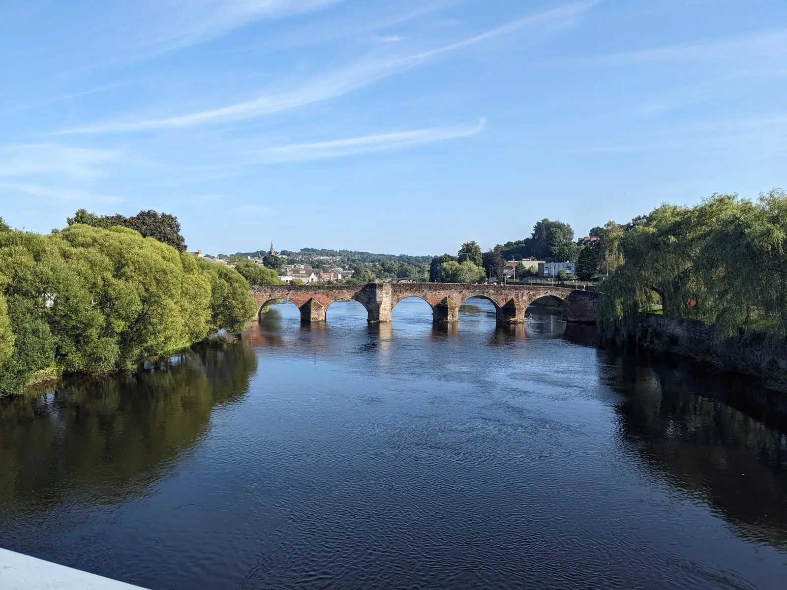 A stone arched bridge crossing a calm river between leafy banks
