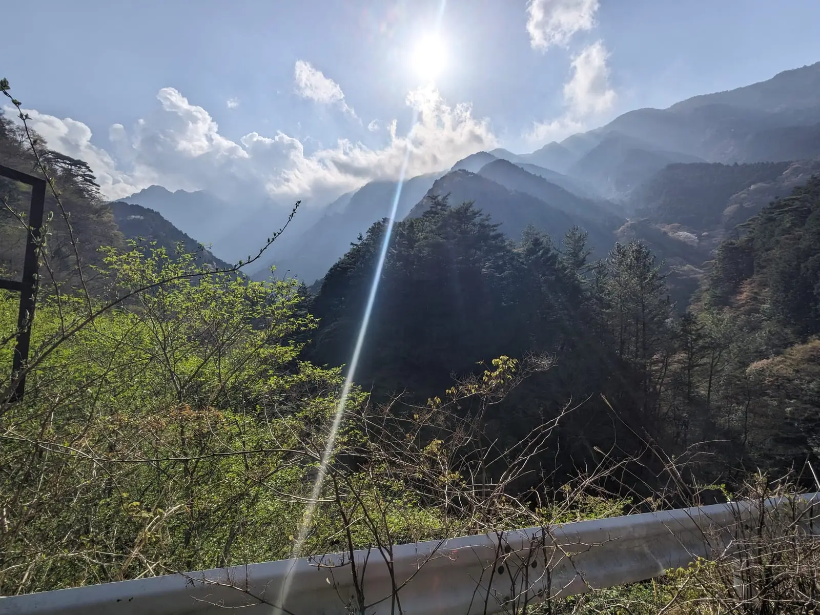 Sun rays breaking through cloud above a forested mountain valley, seen over a guardrail