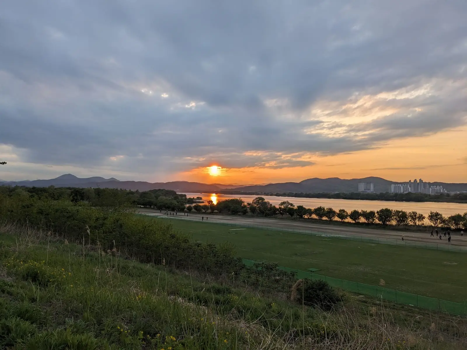 A sunset over a wide river with the Daegu skyline silhouetted along the far bank