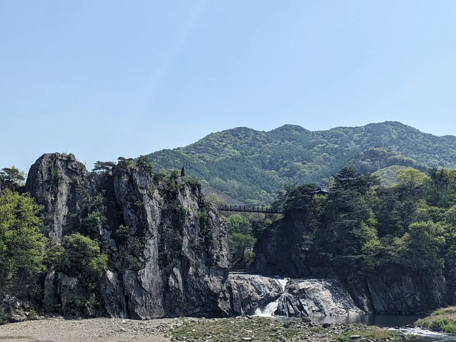 A suspension footbridge crossing between two rocky outcrops above a small waterfall and river