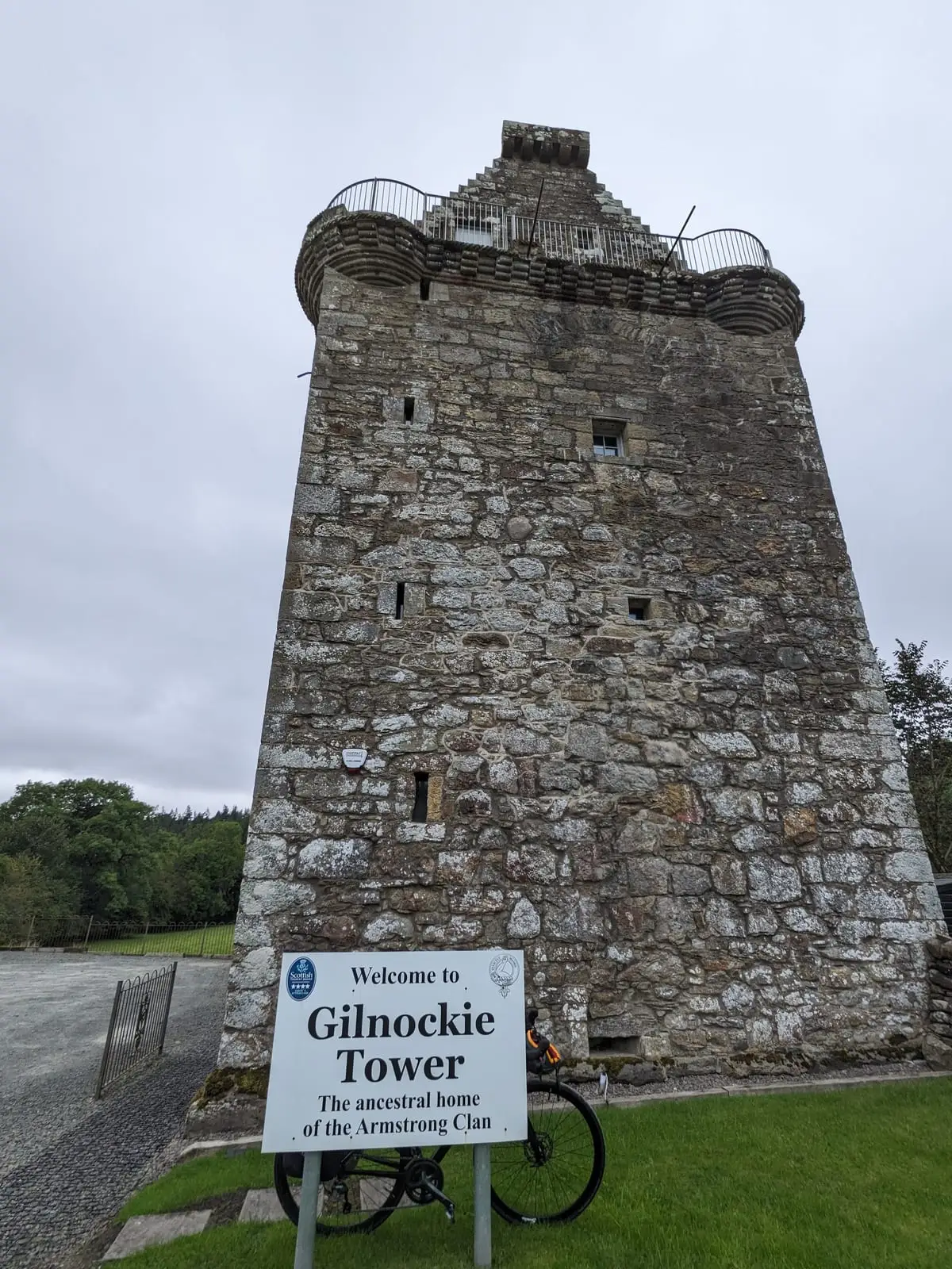 A touring bike leaning beside the entrance sign for Gilnockie Tower