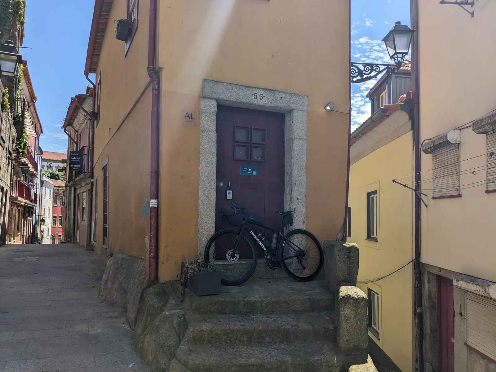 A black touring bicycle leaning outside a yellow building on a steep Porto street