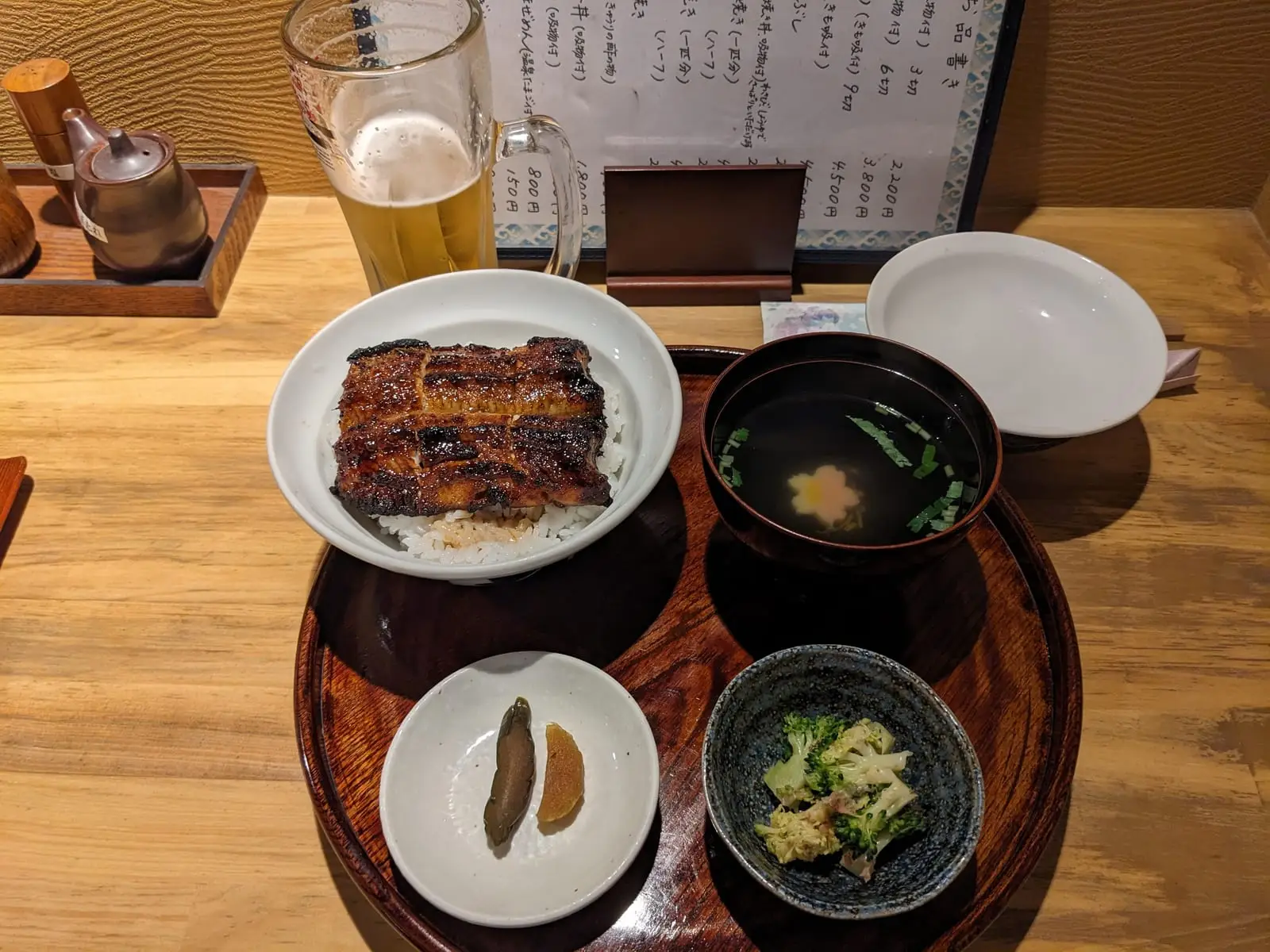 A Japanese set meal with grilled eel, rice, miso soup, and small side dishes, alongside a drink