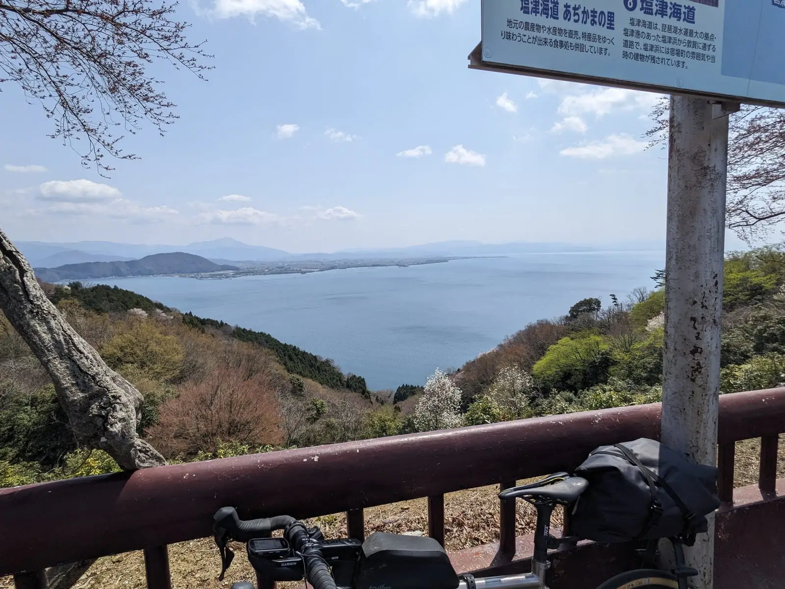 A bike with reduced luggage resting at a railing, overlooking Lake Biwa from a high viewpoint