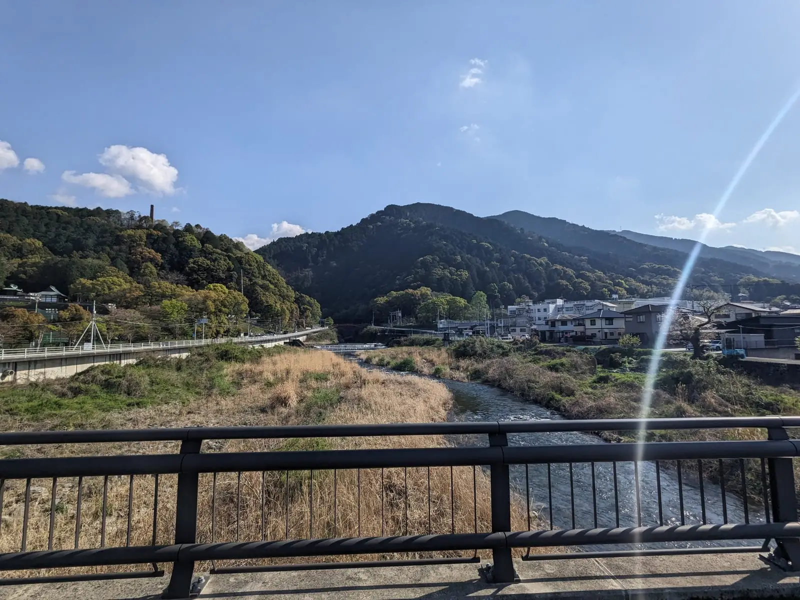 A view from a bridge railing down over a river valley town, with hills and hazy sun beyond