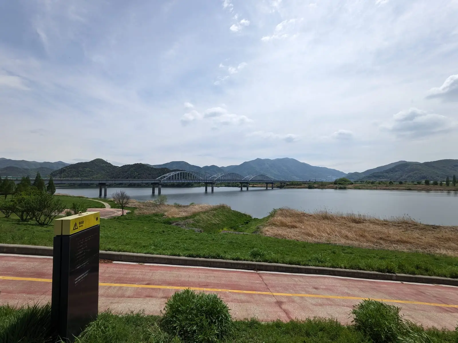 A wide river view with a distant bridge, seen from a signposted riverside cycle path