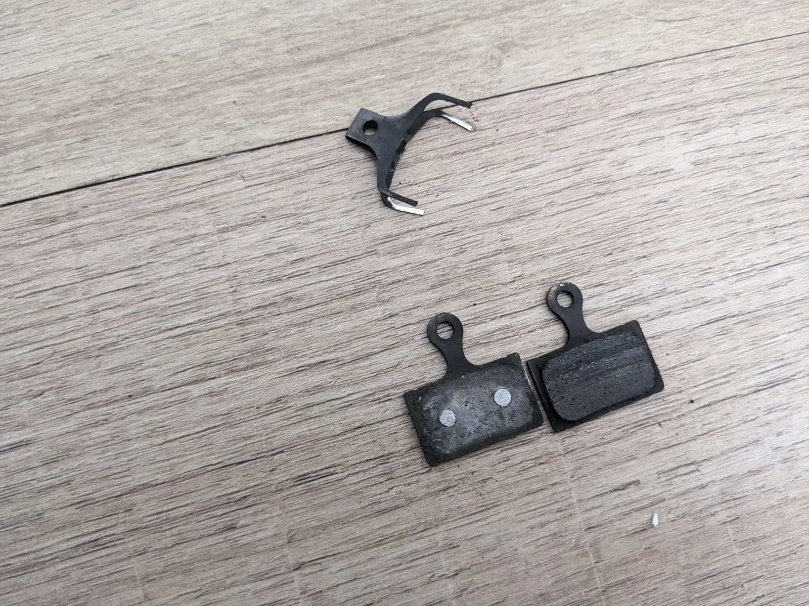A worn bicycle disc brake pad beside its replacement and retaining spring